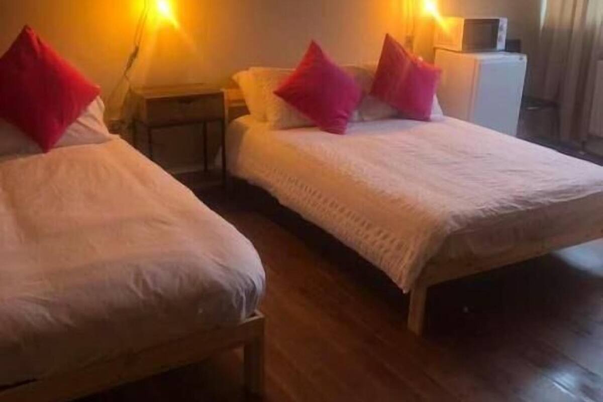 Quarto de hotel com duas camas, cada uma com almofada vermelha, cabeceiras de madeira e abajures.