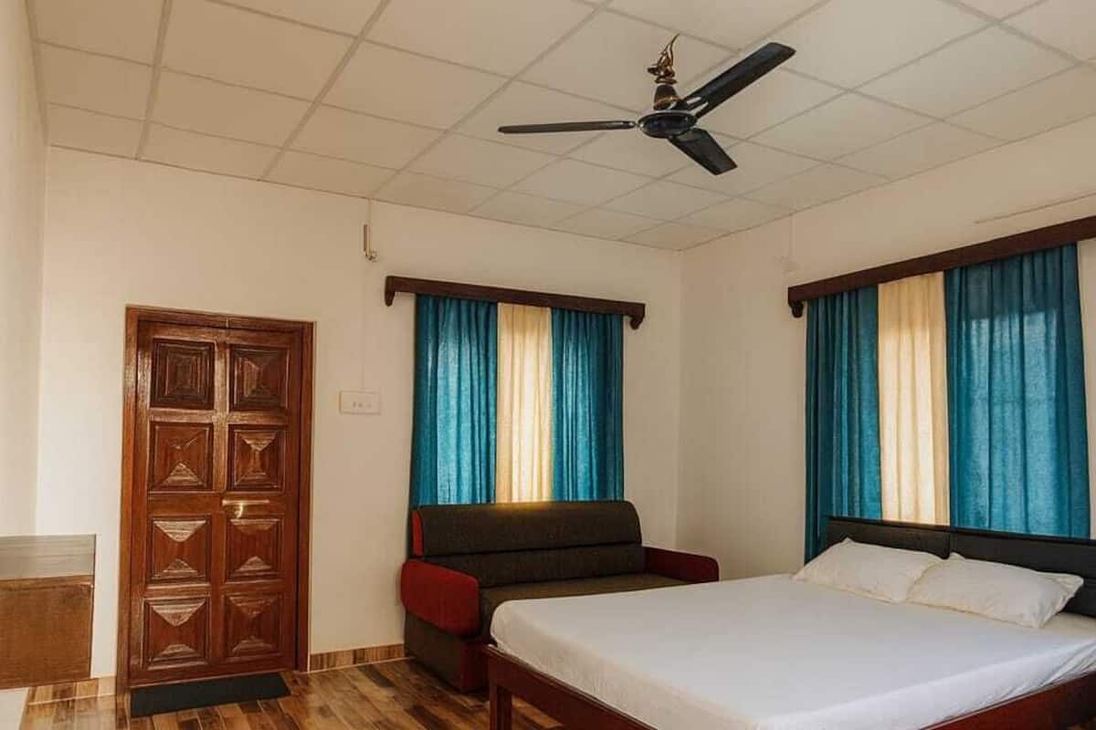 Une chambre d’hôtel avec un plancher en bois, un lit, un canapé, un ventilateur de plafond et des rideaux.