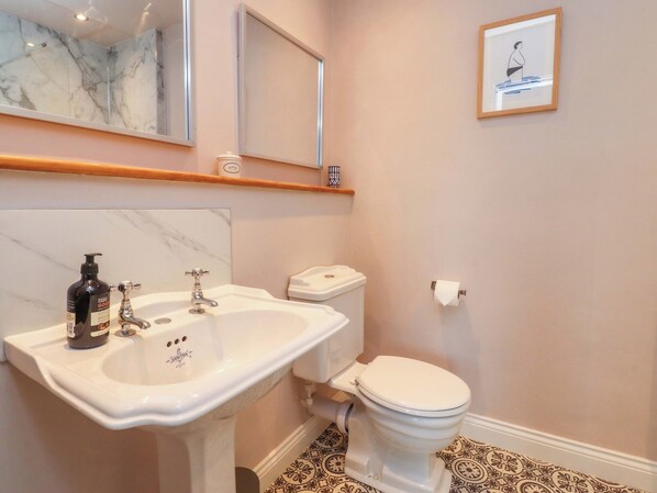 A bathroom with a white sink, a toilet, a mirror, and a framed picture on the wall. - Kirk Yett (Skipton)