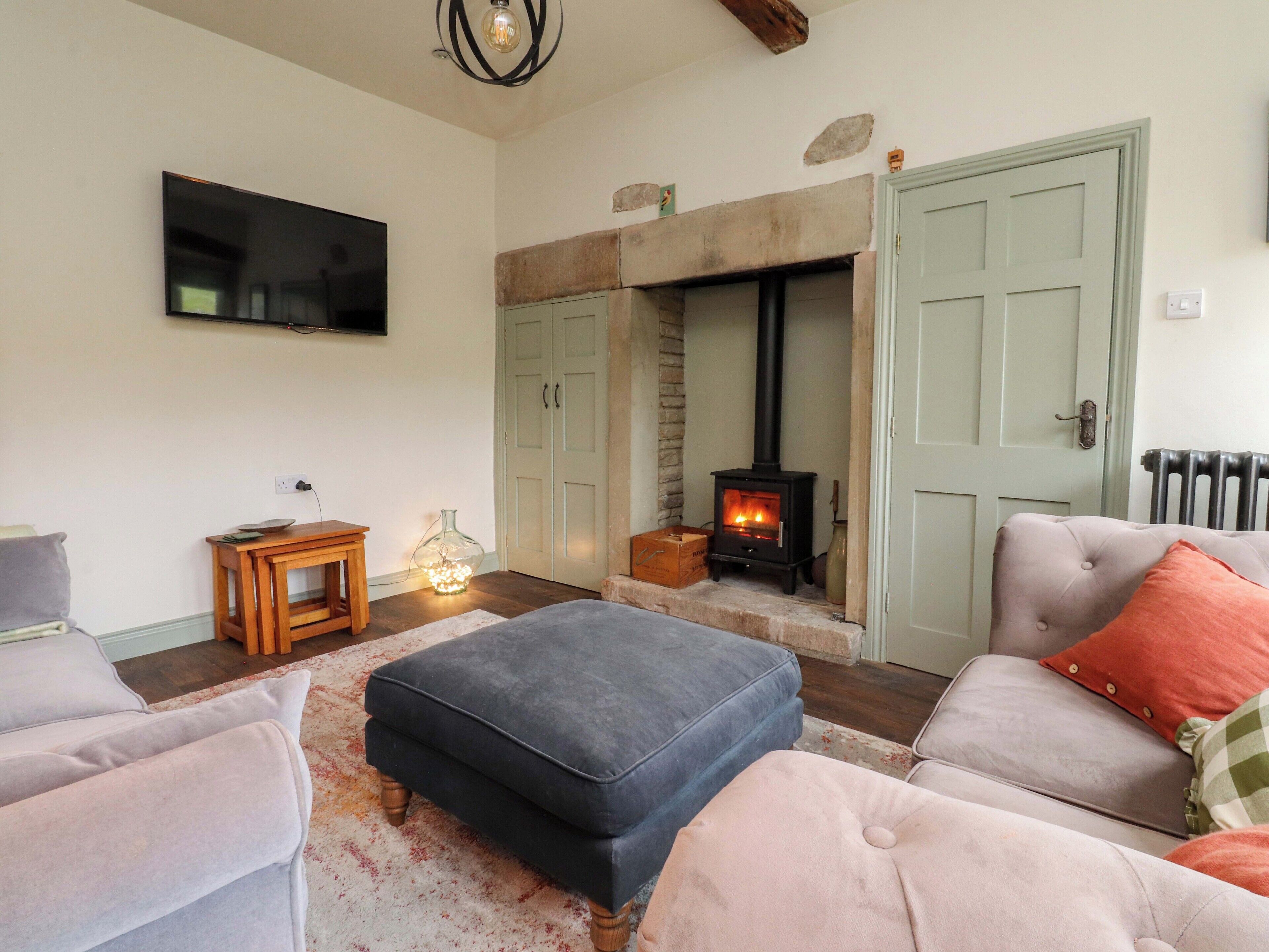 A living room with a fireplace, a television mounted on the wall, and a cozy seating area with an ottoman and two armchairs.