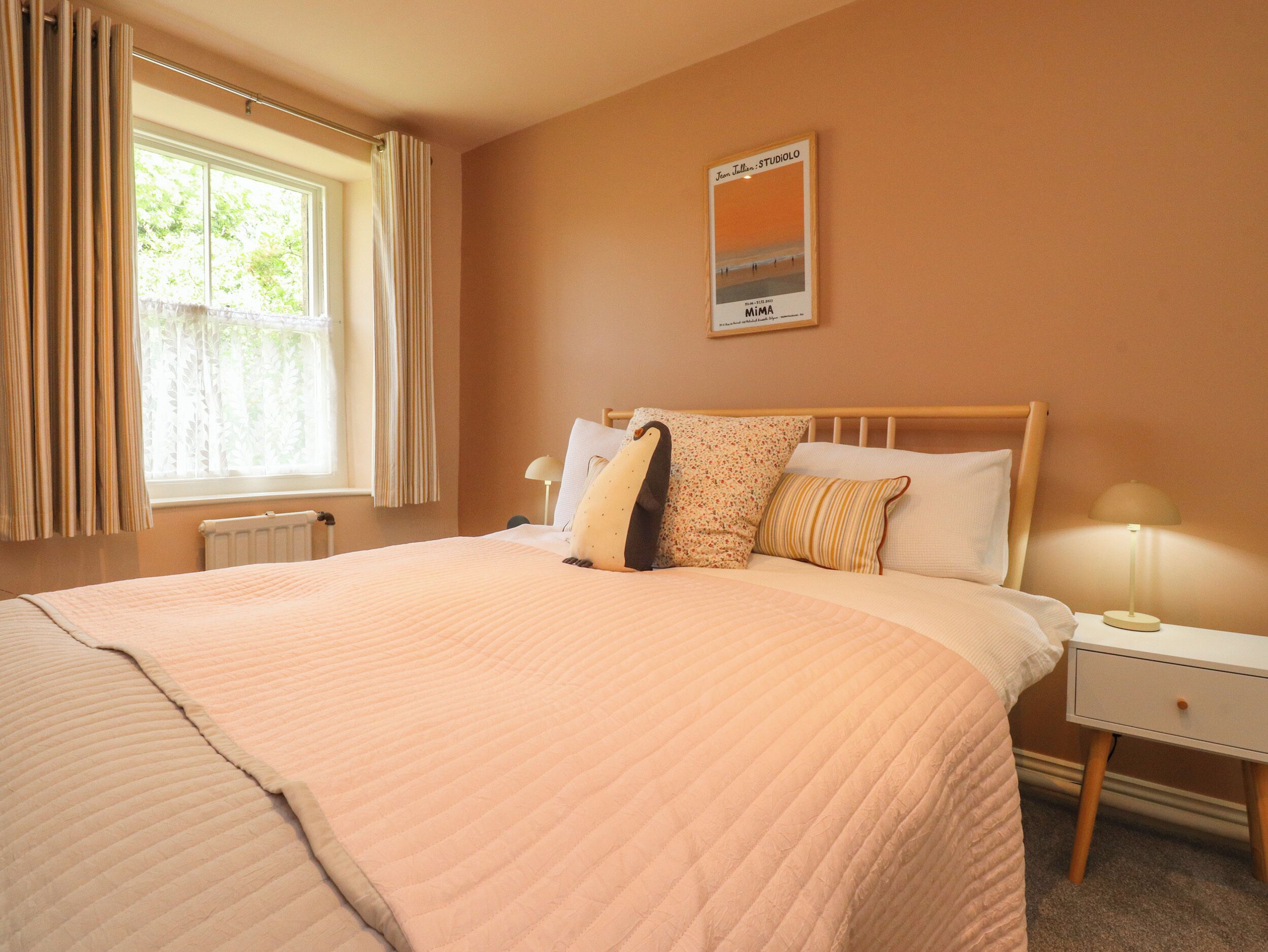 Quarto de hotel com cama, mesa de cabeceira, luminária, janela com cortinas e um quadro pendurado na parede.