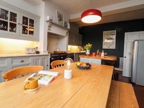 A kitchen with a wooden dining table, a coffee table, and a bowl of fruit. There is a stove, oven, and refrigerator in the kitchen. - Kirk Yett (Skipton)