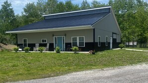 Een huis met twee verdiepingen, een schuin dak, een veranda met stoelen en een grindpad.