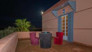 An outdoor patio with a table and chairs, a palm tree, and a building with a blue door. - Mumtaz Dar - Suite Deluxe 3 (Ouahat Sidi Brahim)