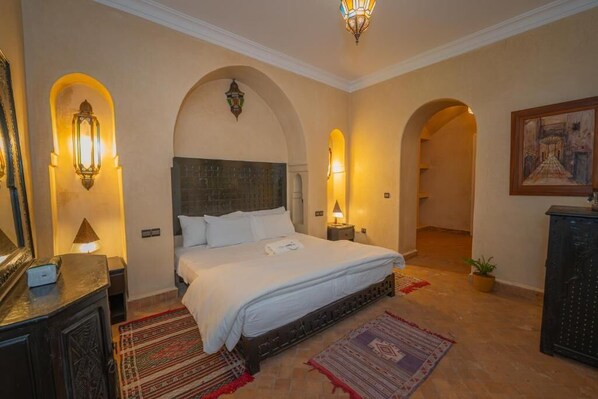 Habitación de hotel con una cama grande, dos lámparas de noche, una mesita de noche, un aparador y un cuadro en la pared.