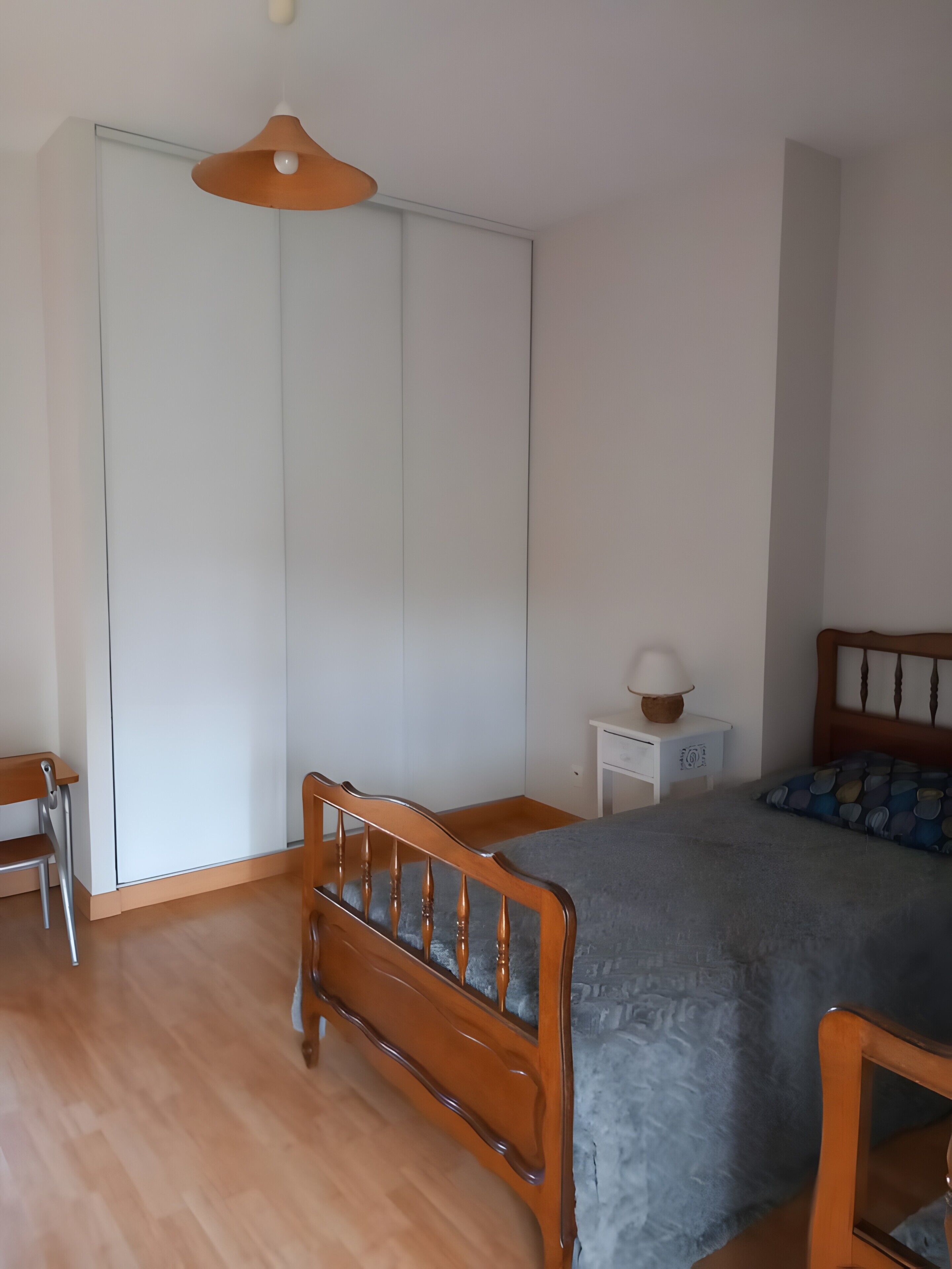 Una camera da letto con un letto di legno, un comodino, una sedia, un armadio e un lampadario.