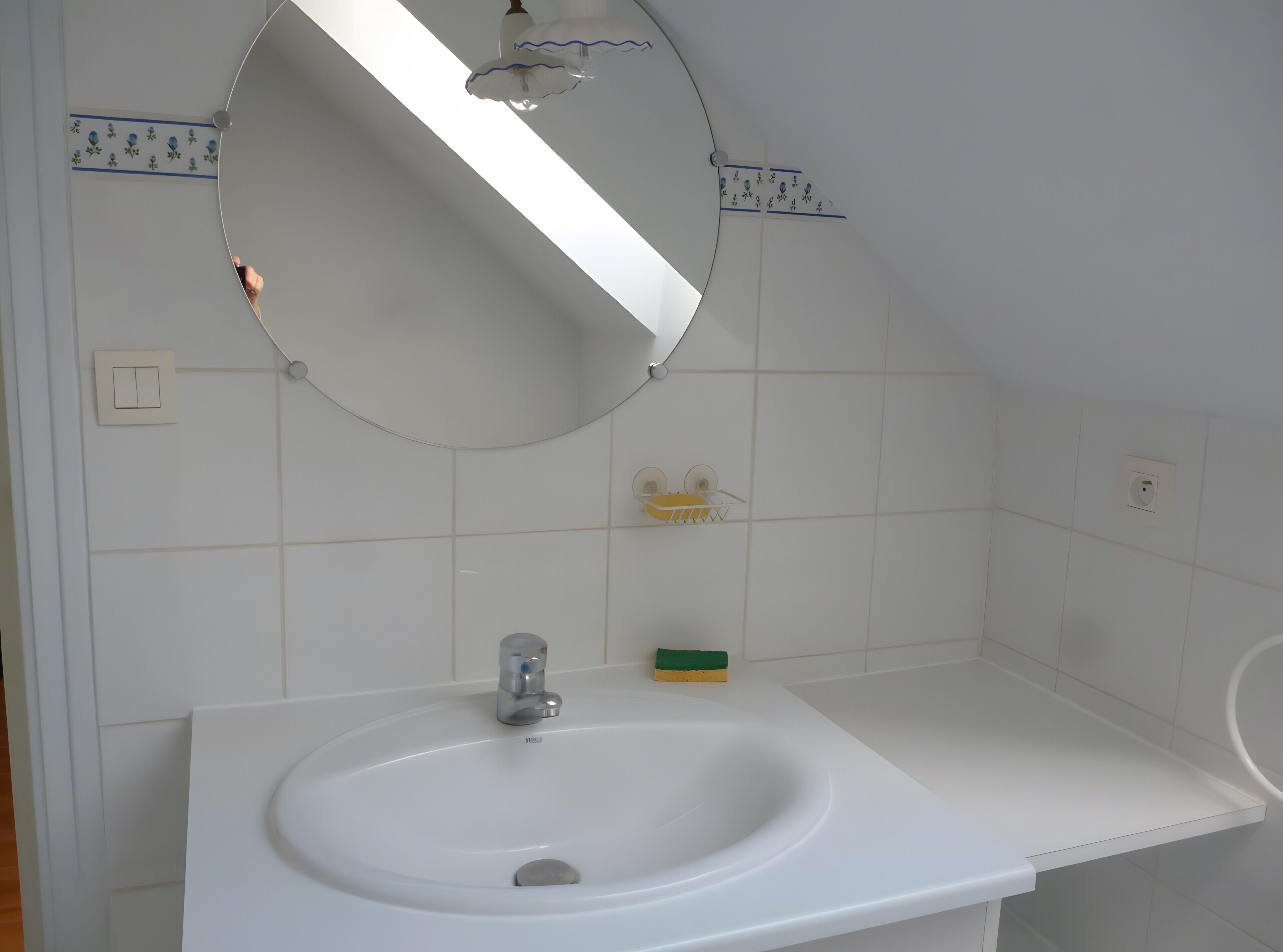 Un bagno con un lavandino bianco, uno specchio e un portascopevoli.