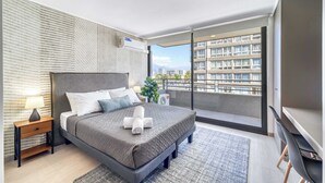 Ein modernes Schlafzimmer mit einem großen Bett, einem Nachttisch mit Lampe, Blick auf eine Stadtlandschaft durch einen Balkon und einem Flachbildfernseher.