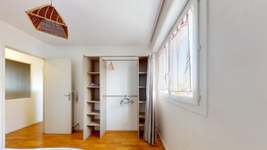 Un armario con estantes y espacio para colgar, una cama con colcha a rayas y una ventana con cortinas.