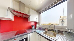 Una cocina moderna con armarios blancos, salpicadero rojo, electrodomésticos de acero inoxidable y una ventana con vistas a edificios.