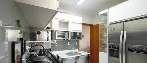 Una cocina compacta con microondas integrado, refrigerador y un pequeño comedor con mesa y sillas.