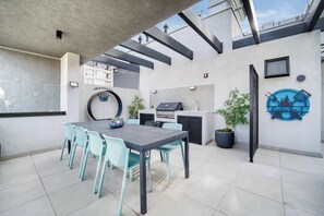 Un área de patio al aire libre con una mesa y sillas para comer, una parrilla y una planta en maceta.