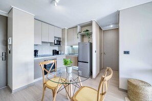 Eine moderne Küche mit weißen Schränken, einem Edelstahl-Kühlschrank und einem Glastisch mit zwei Stühlen.