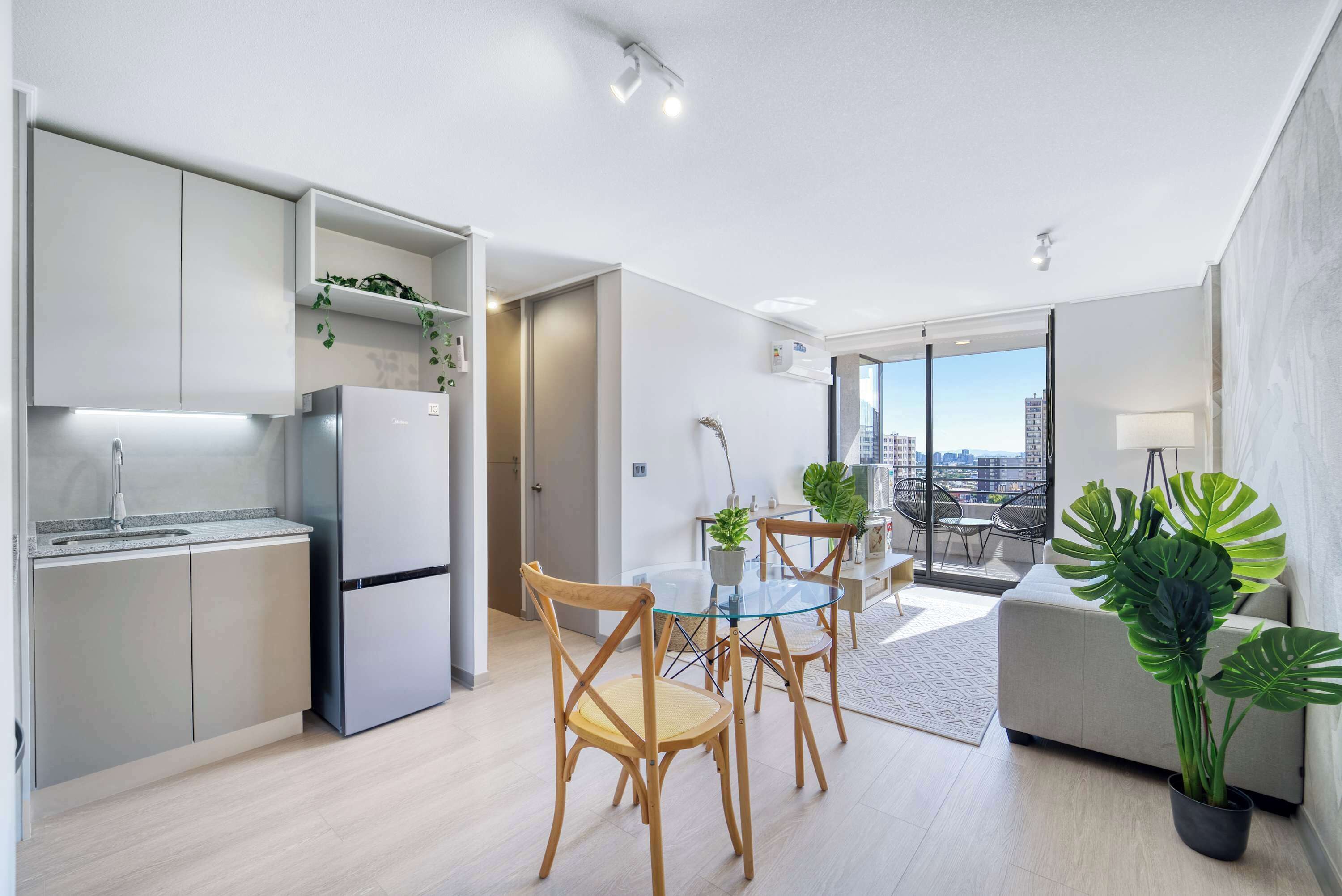 A modern apartment with a kitchen, dining area, and living room. It features a large window with a city view, a dining table with chairs, and a sofa.