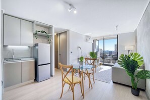 Eine moderne Wohnung mit Küche, Essbereich und Wohnzimmer. Sie verfügt über ein großes Fenster mit Blick auf die Stadt, einen Esstisch mit Stühlen und ein Sofa.