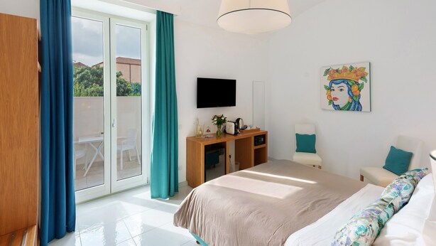 Une chambre d’hôtel équipée d’un lit, d’un bureau, d’une chaise, d’une télévision et d’une porte-fenêtre coulissante donnant sur l’extérieur.
