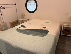 A bedroom with a bed, a round window, a nightstand, a lamp, and a wall-mounted shelf. - Villa 'Corinne' with Private Terrace, Wi-Fi and Air Conditioning (Sainte-Marie-la-Mer)