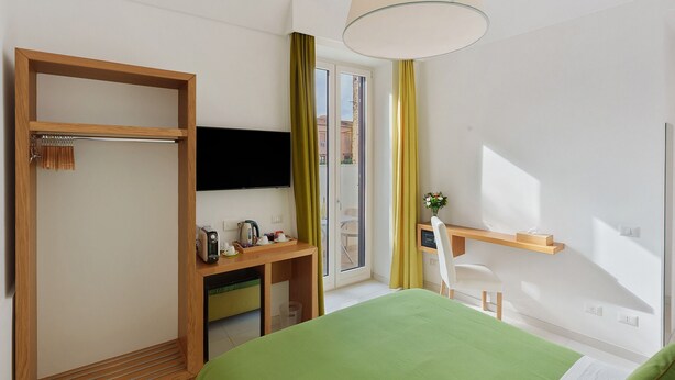 Une chambre d’hôtel comprenant un lit, un bureau avec une chaise, une télévision, une fenêtre avec des rideaux et une porte avec un porte-manteau.