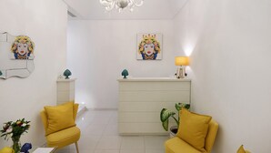 Un salon moderne avec un comptoir d’accueil blanc, des fauteuils jaunes, un lustre et des œuvres d’art accrochées aux murs.