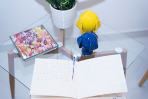 Une table en verre sur laquelle se trouvent un carnet, un stylo, une plante en pot et un objet décoratif.