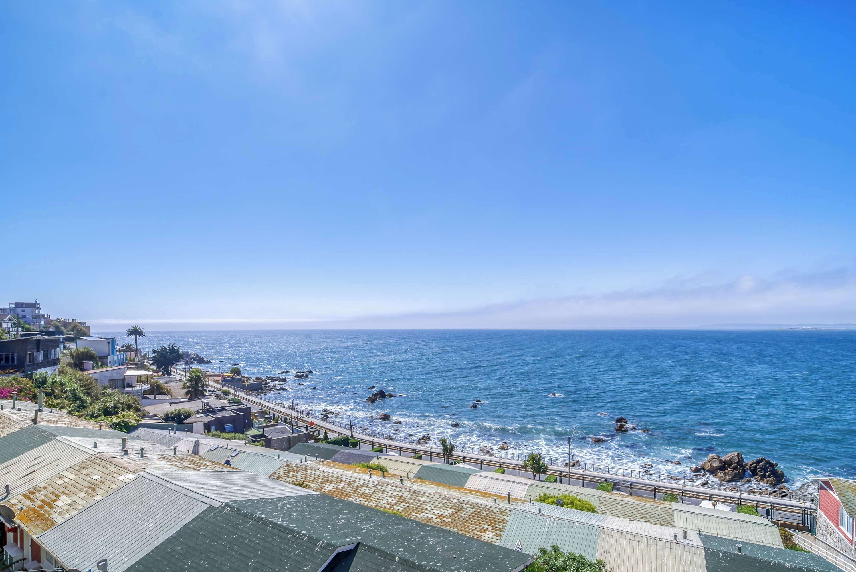 Vista costera amb un passeig pavimentat al costat de la platja, edificis amb terrasses i l'oceà al fons.