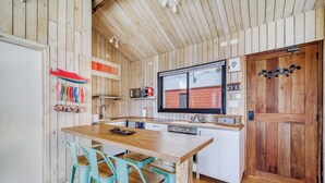Ett kök med träpanel på väggarna, en köksö i trä med barstolar, ett stort fönster och en tegelvägg som syns genom fönstret.