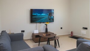 Un salón moderno con un televisor de pantalla plana grande montado en la pared, una mesa de centro con un jarrón y un libro, y un sofá.