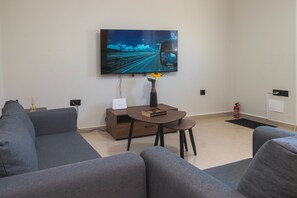 Ein modernes Wohnzimmer mit einem großen Flachbildfernseher an der Wand, einem Couchtisch mit Vase und Buch sowie einer Couch.