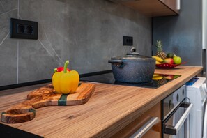 Eine Küchenarbeitsplatte mit Schneidebrett, einem gelben Paprika, einem Topf und einer Obstschale.