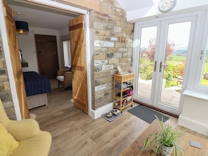A cozy room with a wooden door leading to a balcony, a wicker chair, a wooden bench, and a potted plant. - Eastend Cottage (Leyburn)