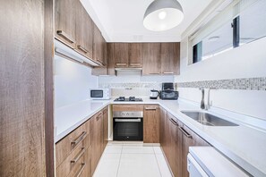A modern kitchen with wooden cabinets, a built-in oven, a microwave, a coffee maker, and a sink. - Cochoa View- 3D Frente al Mar (Concón)