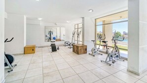 Ett rymligt gym med olika typer av träningsutrustning, stora fönster och utsikt över omgivningen.