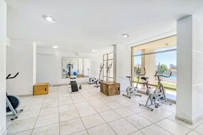 A spacious gym with various exercise equipment, large windows, and a view of the outdoors. - Comfort Life Concón- 3D with Wifi (Concón)
