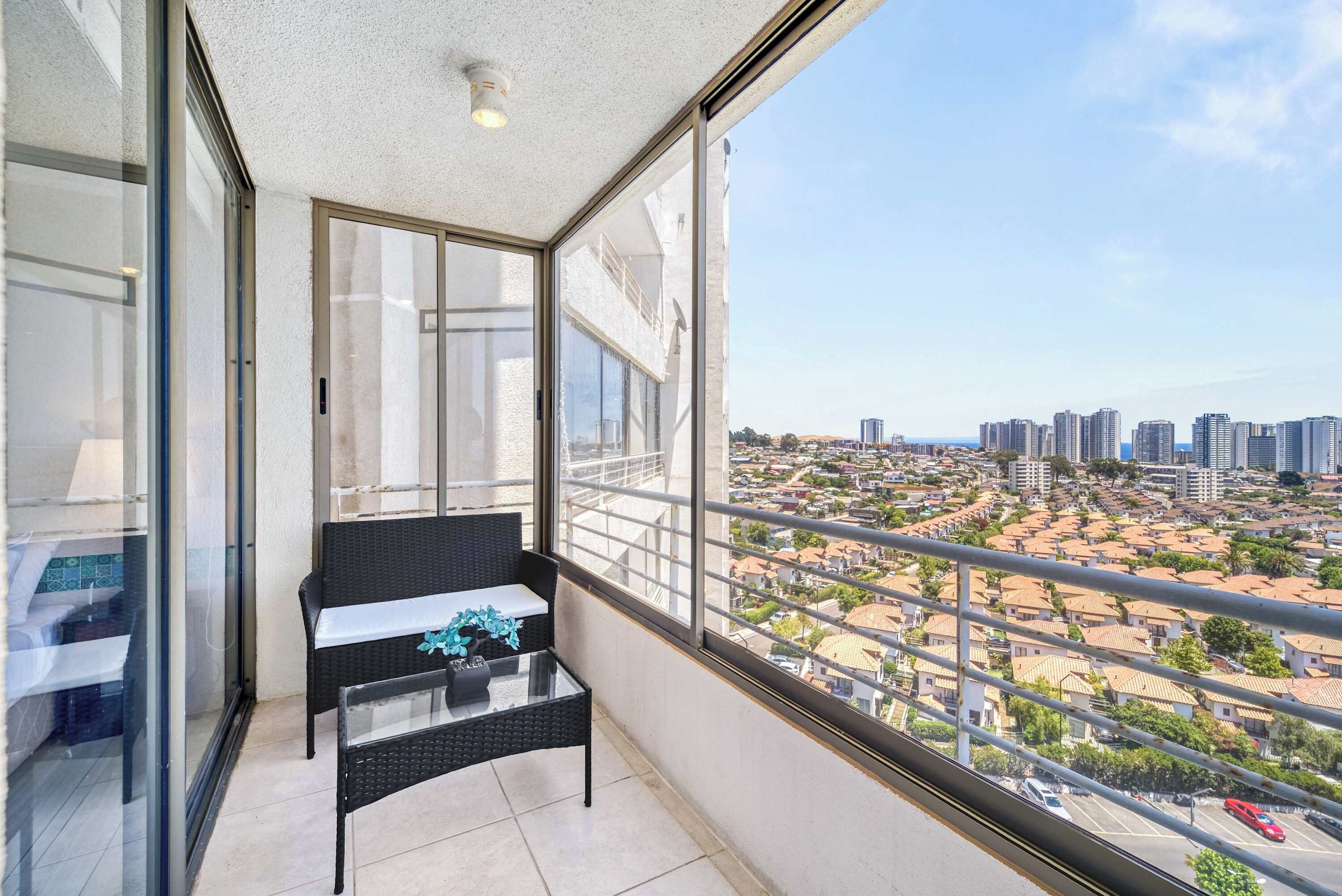 A balcony with a glass door, a black wicker sofa, and a view of a cityscape.