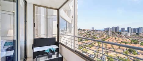 A balcony with a glass door, a black wicker sofa, and a view of a cityscape.
