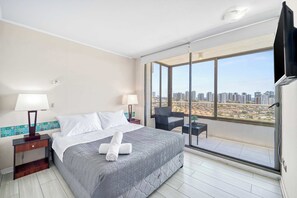Une chambre d’hôtel avec un grand lit, deux tables de chevet avec des lampes, un balcon offrant une vue sur la ville et un téléviseur fixé au mur.