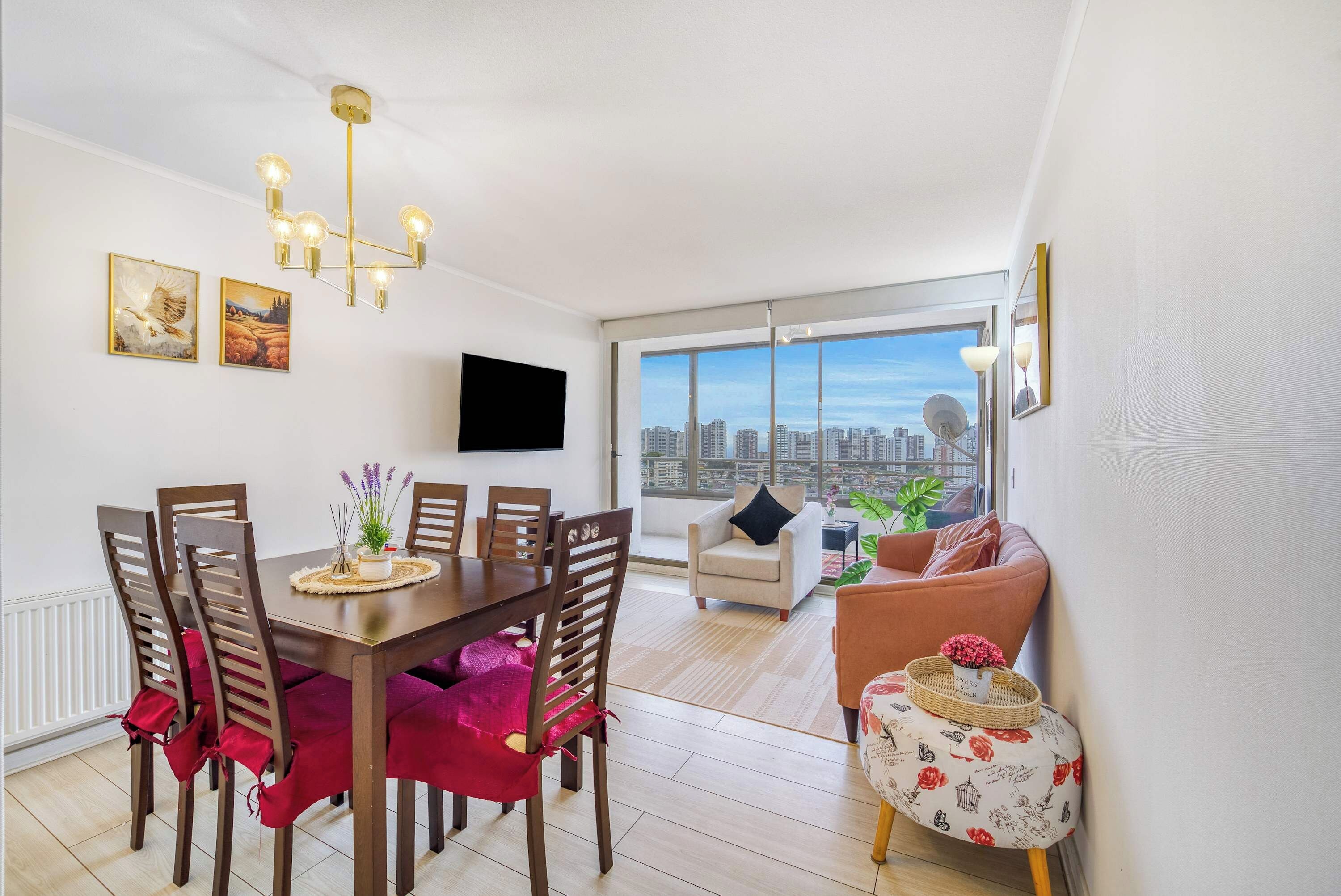 Un salon moderne comprenant un coin repas, une grande fenêtre offrant une vue sur la ville et un téléviseur à écran plat fixé au mur.