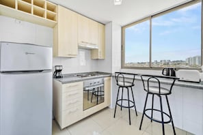 A modern kitchen with white cabinets, a built-in oven, a stove, and a large window offering a city view. - Comfort Life Concón- 3D with Wifi (Concón)