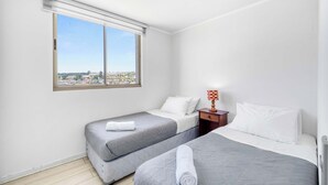 Ett hotellrum med två sängar, ett fönster med utsikt över stadsbilden och ett litet bord med en lampa.