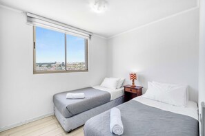 A hotel room with two beds, a window with a view of a cityscape, and a small table with a lamp. - Comfort Life Concón- 3D with Wifi (Concón)