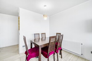Un espace repas comprenant une table et des chaises en bois, des murs blancs et un luminaire au plafond.