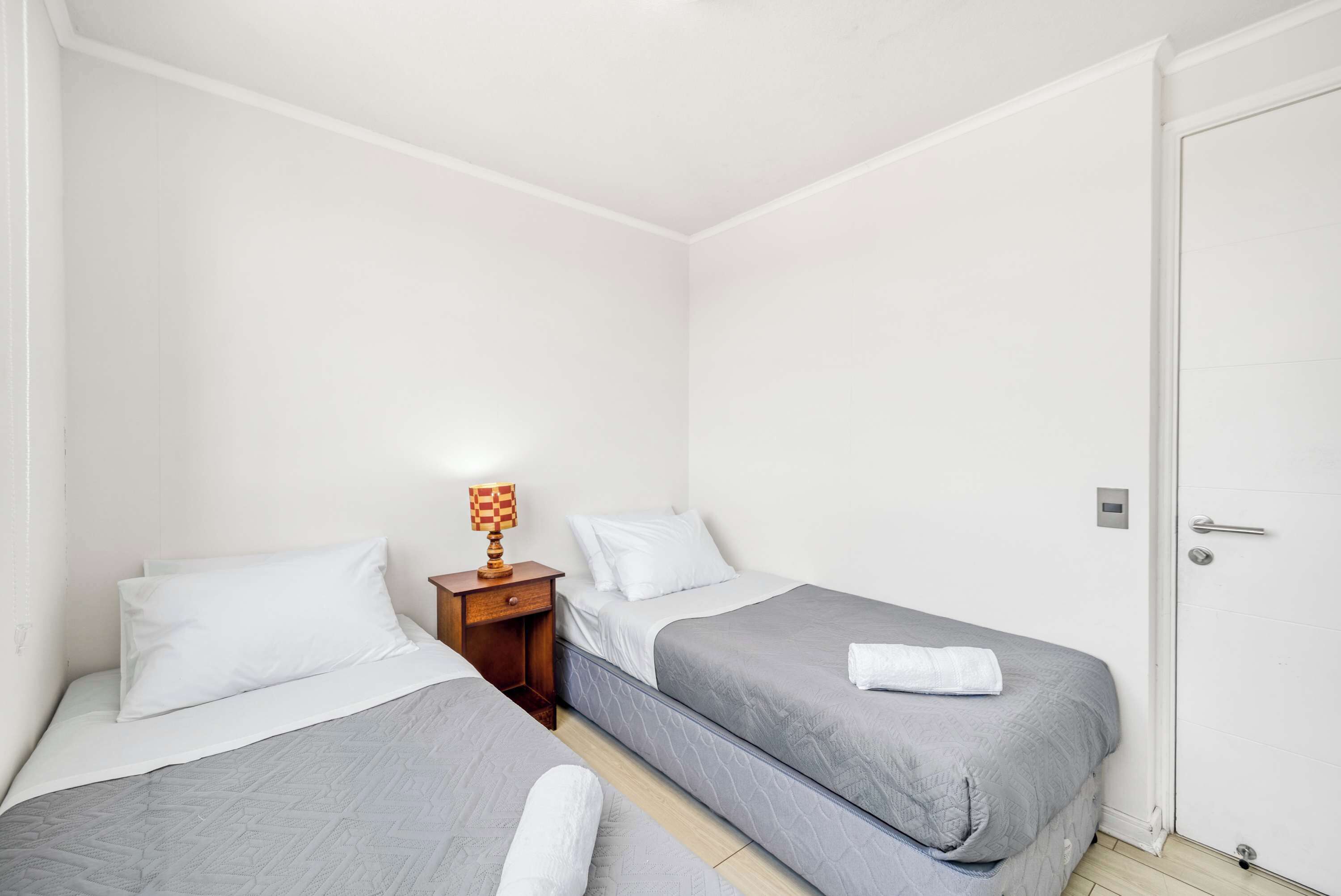 A room with two single beds, a nightstand with a lamp, and a white door.