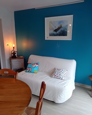 A room with a white sofa, a blue wall, a framed picture, a table with chairs, and a small bedside table with a lamp. - Maison Le Clos des Ânes: private terrace and garden in Sainte-Marguerite sur Duclair (Sainte-Marguerite-sur-Duclair)