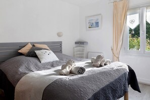 A bedroom with a bed, pillows, a bedside table, a wall-mounted lamp, and a window with curtains.