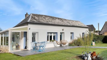Een huis met een witte gevel, rieten dak en een overdekt terras met blauwe stoelen.
