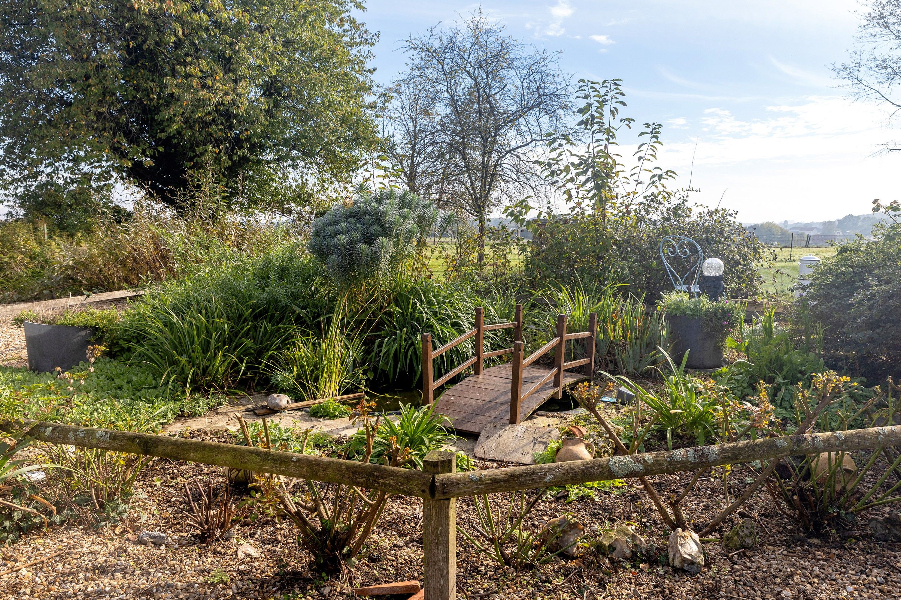 Un jardin avec un pont en bois, différentes plantes et une sculpture en métal.