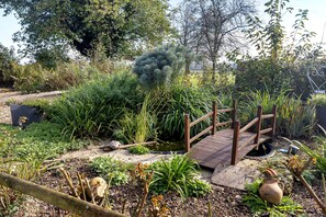 A garden with a wooden bridge, various plants, and a stone pathway.