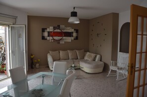 A living room with a glass dining table, beige sofa, and a white rocking chair. - IL SOGNO MODERNO (Caltagirone)