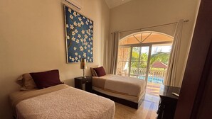 Camera d'albergo con due letti, un comodino, una lampada e un'ampia finestra vista piscina e vegetazione.