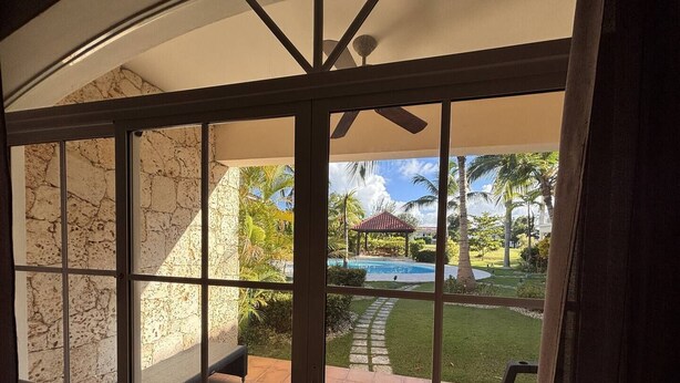 Vista attraverso una porta di vetro su un patio con piscina, mobili da esterno e un gazebo.